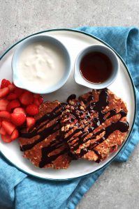 Pancakes de fresa y avena servidos con jarabe de arce, yogurt y fresas picadas